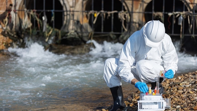 Worker in protective gear collecting water samples for contamination testing